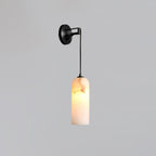 Vaelara alabaster wall sconce in the black finish, lit, with the cord dropping to the stone shade