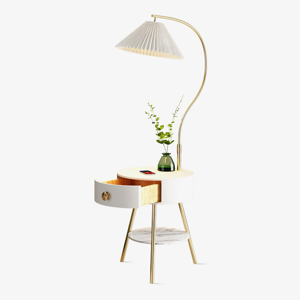 A Clérachic floor lamp arches its pleated white shade over a built-in round nightstand with a drawer, styled here with a small vase of greenery on top.