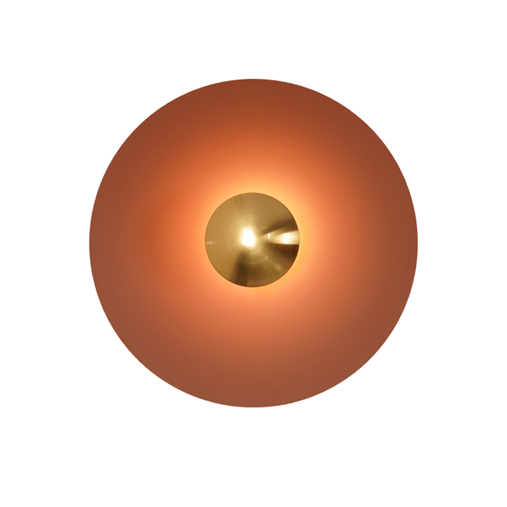 A deep bronze-brown Clérachic wall light glows warm on white, its antique copper centre bright at its core.