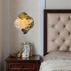 Above a dark wood nightstand holding a framed photo and small figurine, this Clérachic wall light glows beside a tufted headboard.