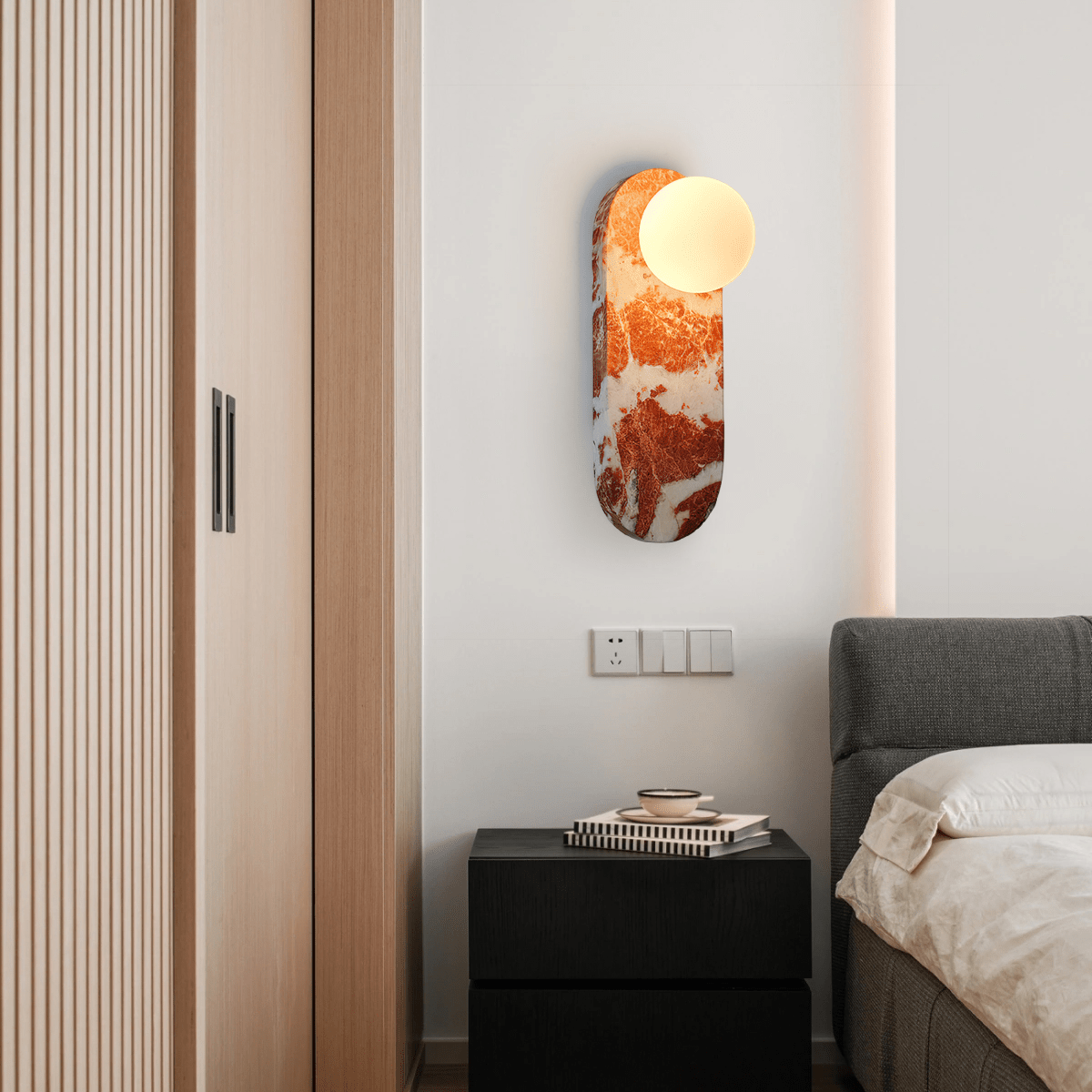 Mounted beside slatted closet doors, the lit Clérachic sconce glows above a nightstand stacked with books.