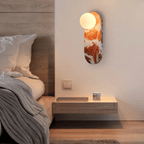In a bedroom, the lit Clérachic sconce hangs above a floating nightstand with a candle and a knit throw.