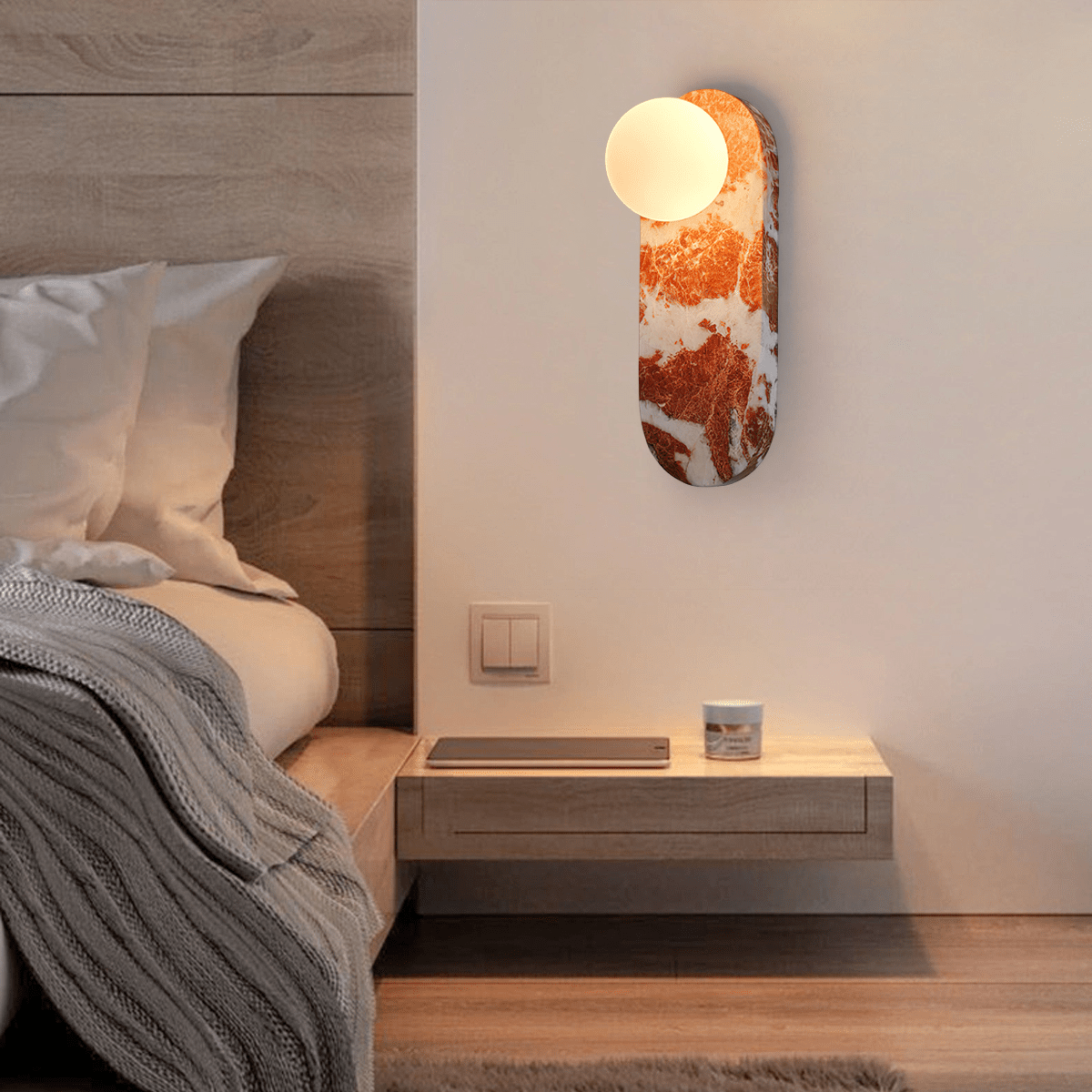 In a bedroom, the lit Clérachic sconce hangs above a floating nightstand with a candle and a knit throw.