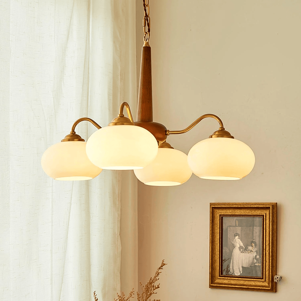 Four cream glass shades on this Clérachic chandelier hang beside a sepia-toned print in a gilt frame.