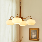 Four cream glass shades on this Clérachic chandelier hang beside a sepia-toned print in a gilt frame.