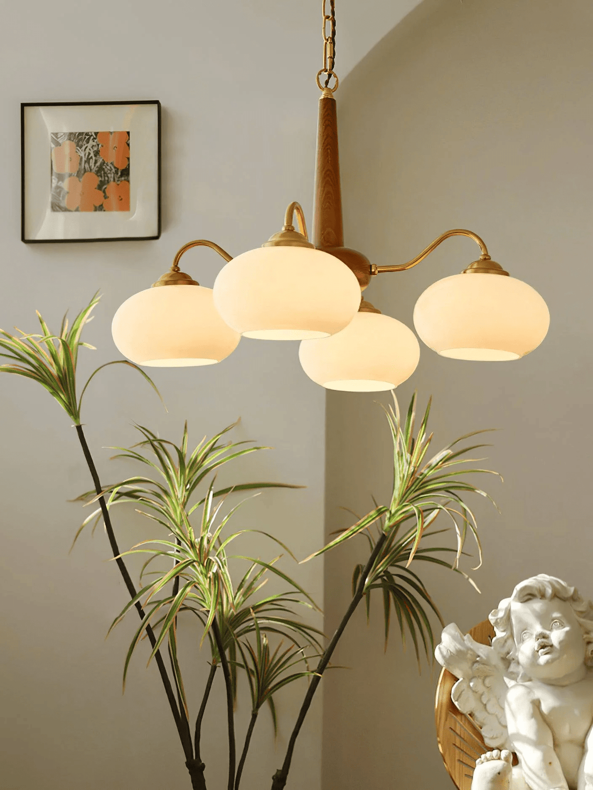 A dracaena plant and a small cherub figure sit beneath this Clérachic chandelier's four cream shades.