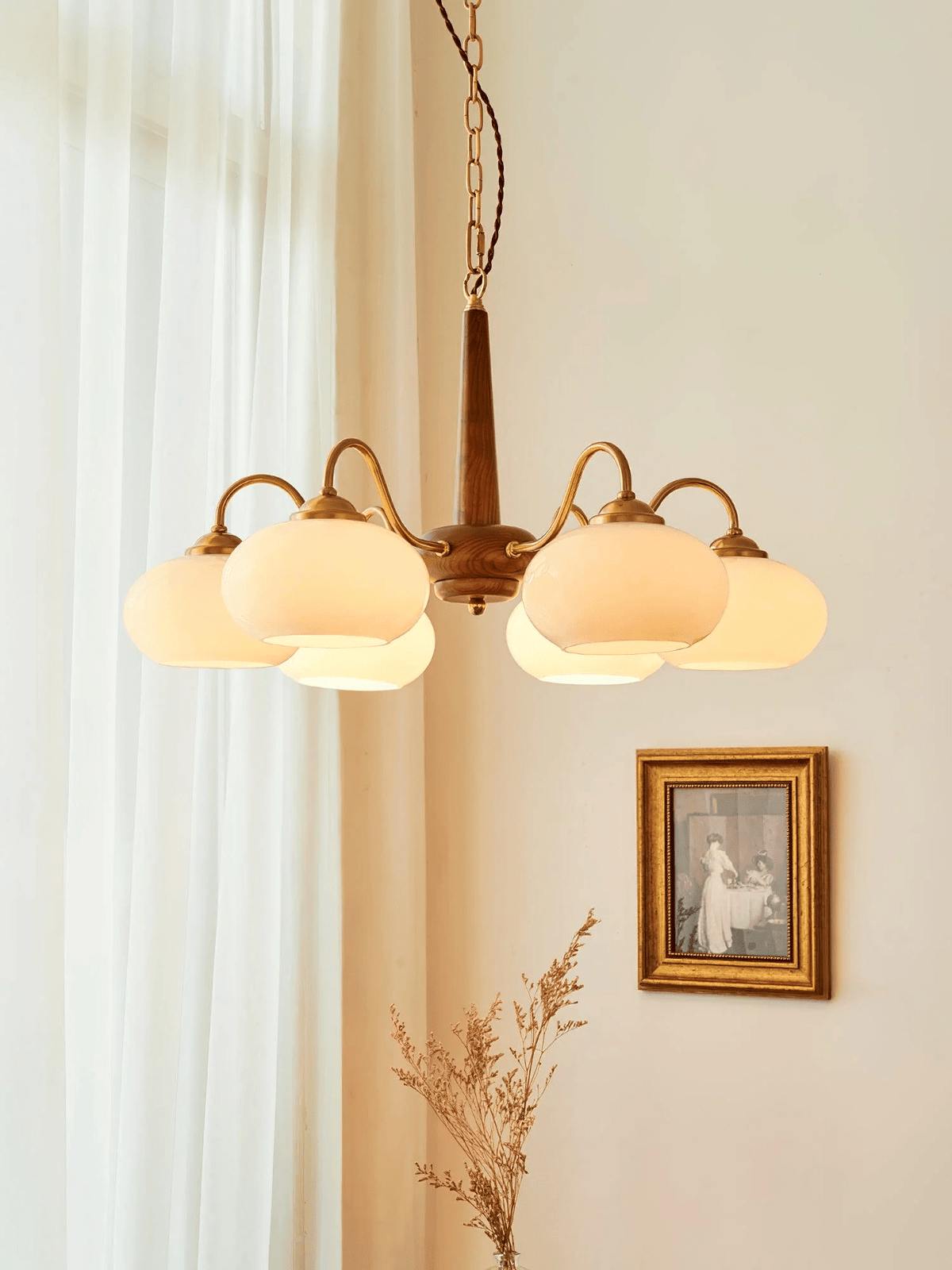 Sheer curtains and a small gilt-framed print flank this Clérachic chandelier's six cream glass shades.