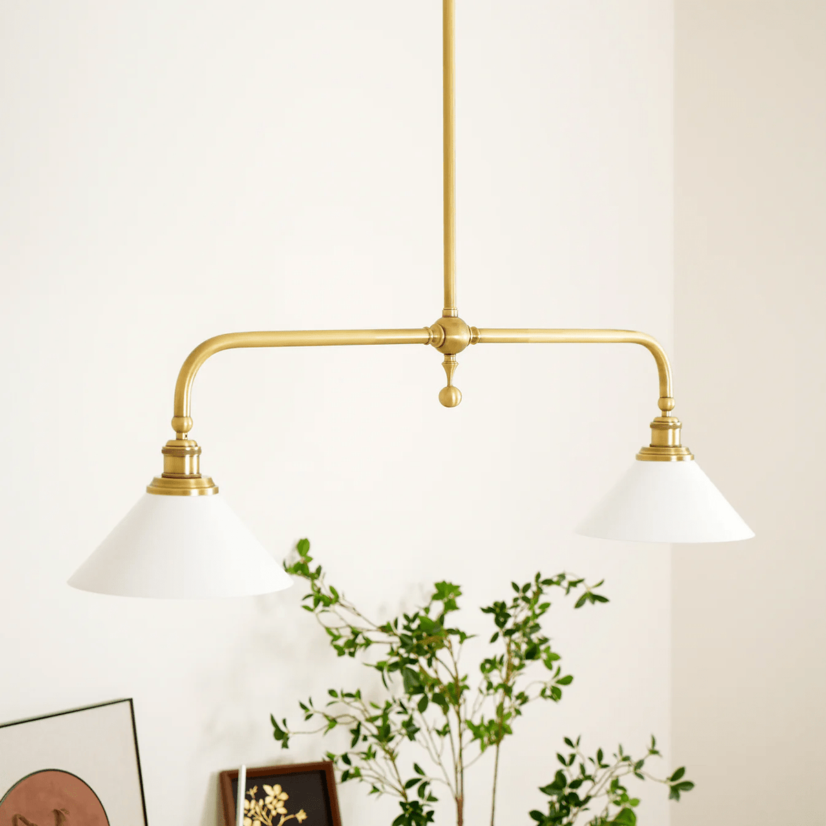 A framed print and trailing plant style the console table below this Clérachic pendant, glowing warm against the wall.