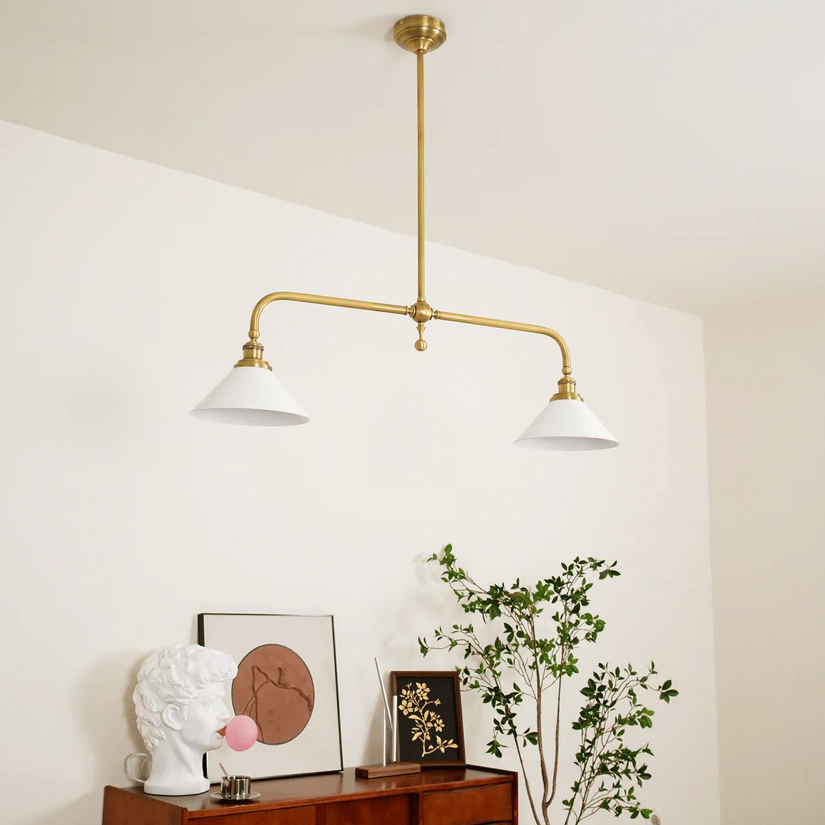 Angled against a cream wall, this Clérachic pendant glows warm above a console table with art and greenery.
