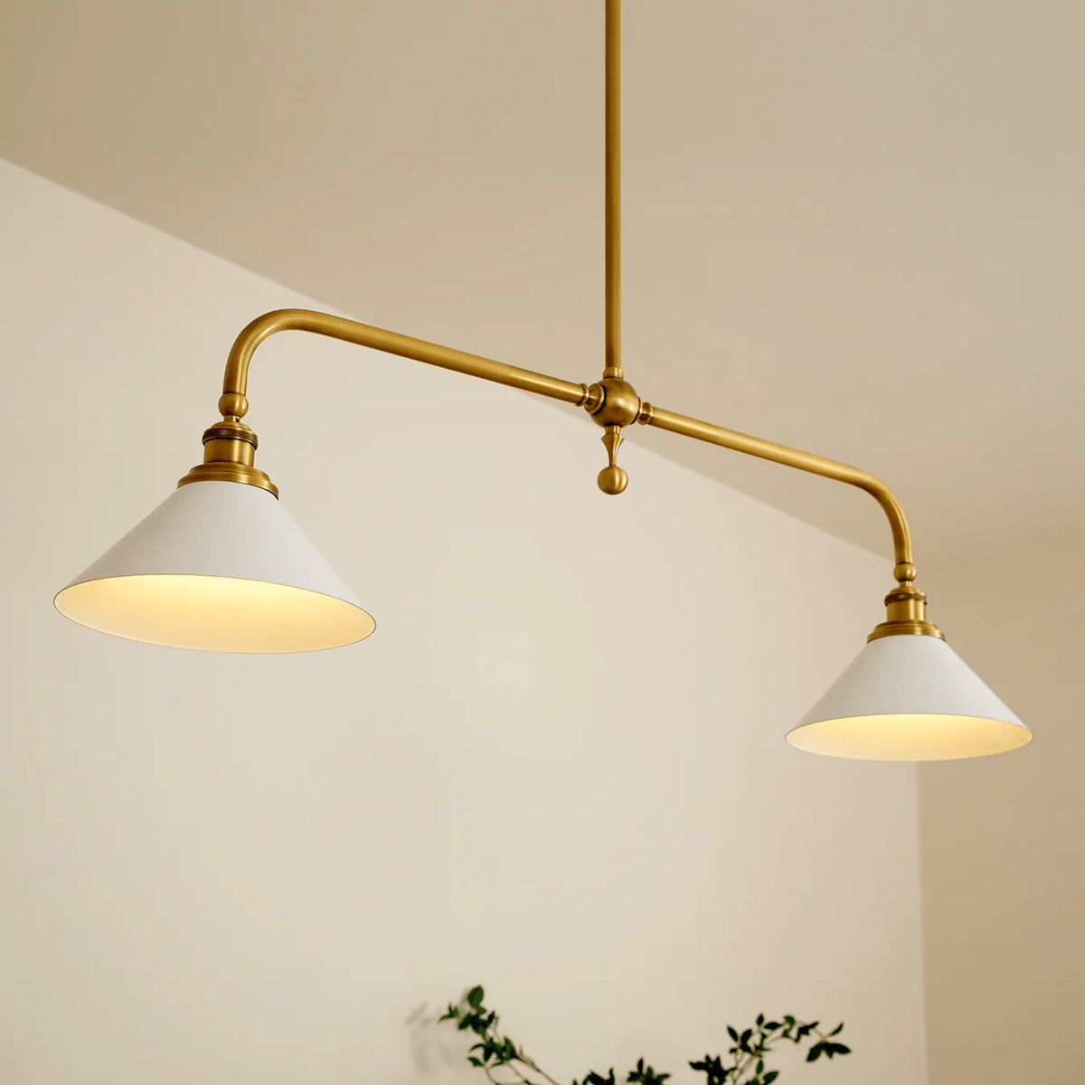 A closer angle on this Clérachic pendant shows both white conical shades glowing warm against a plain cream wall.