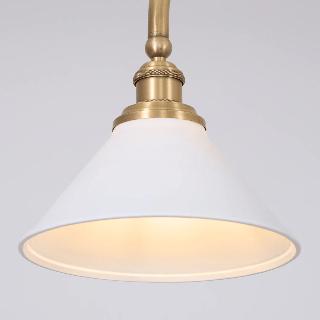 Close view of one shade on this Clérachic pendant, glowing warm beneath its brass elbow arm.