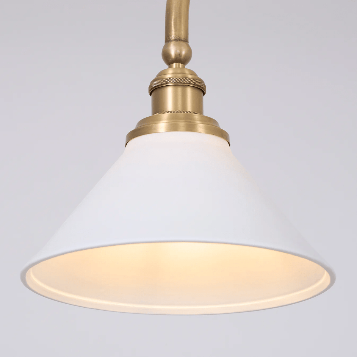 Close view of one shade on this Clérachic pendant, glowing warm beneath its brass elbow arm.