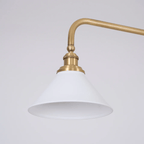 Close view of one white conical shade and its brass elbow arm on this Clérachic pendant, unlit against grey.