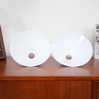 Two white conical shades from this Clérachic pendant rest face-up on a wood dresser, their centre sockets open.