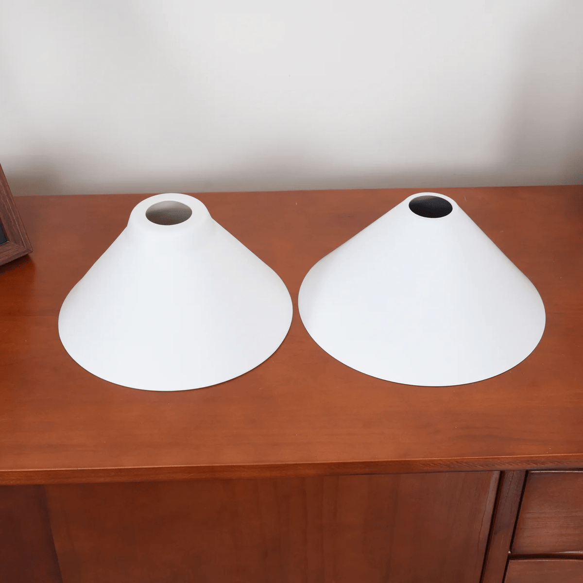 The narrow brass-fitted tops of two shades from this Clérachic pendant face upward on a wood dresser.