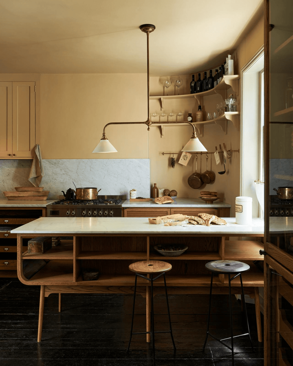 Wood open shelving and bar stools sit beneath this Clérachic pendant, glowing warm above a dark-floored kitchen counter.