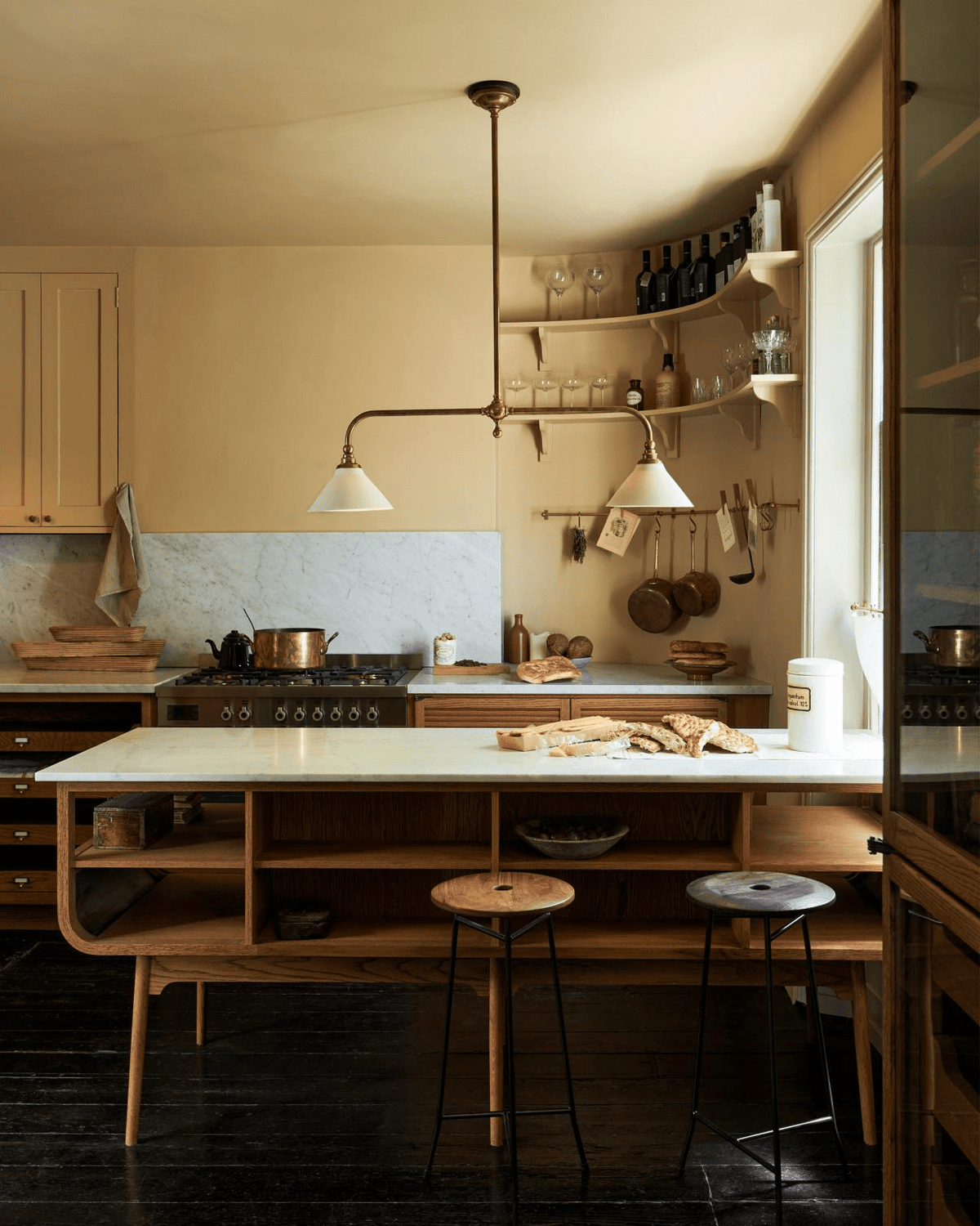 Wood open shelving and bar stools sit beneath this Clérachic pendant, glowing warm above a dark-floored kitchen counter.