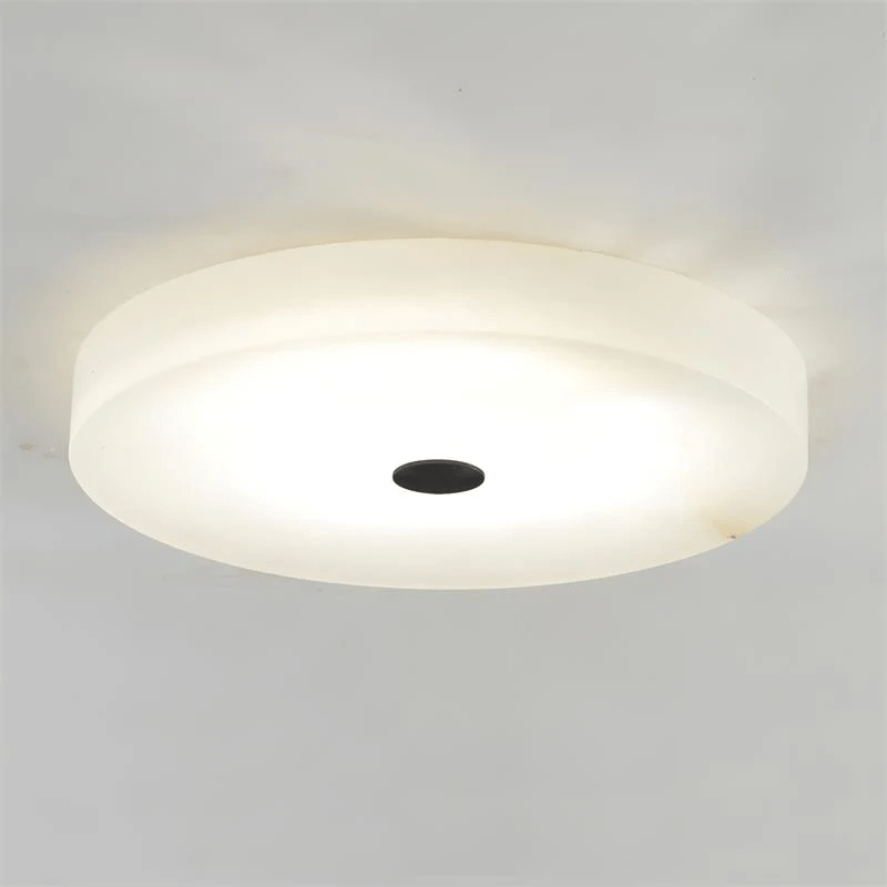 Olaean flush mount on a plain background with its black centre cap and lit alabaster shade.