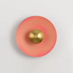Shown on a pale grey backdrop, this bright pink Clérachic wall light glows around an antique copper centre.