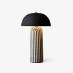 This Clérachic table lamp stands unlit on a plain grey backdrop, its striped ceramic base beneath a matte black dome shade.