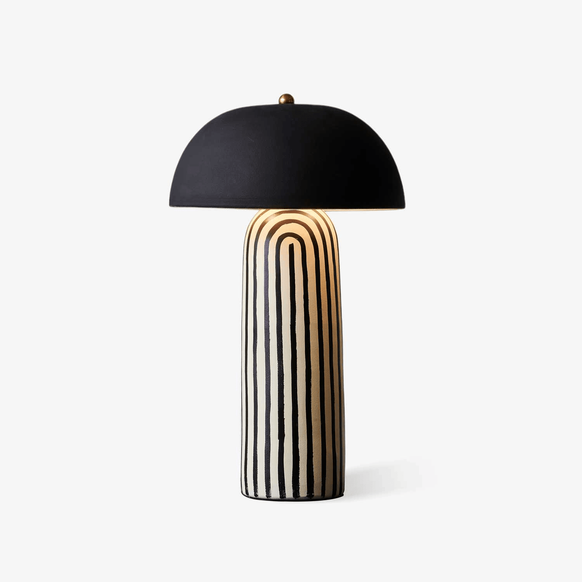 This Clérachic table lamp stands unlit on a plain grey backdrop, its striped ceramic base beneath a matte black dome shade.