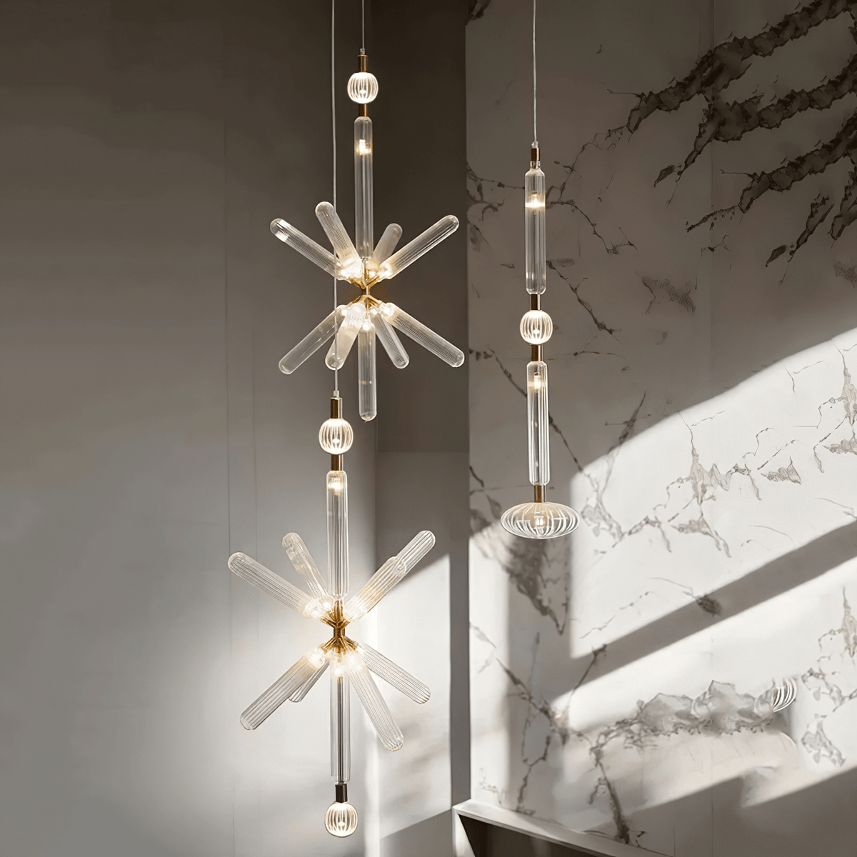 Three Clérachic pendants hang at staggered heights, lit, against a dark stone wall streaked with sunlight.
