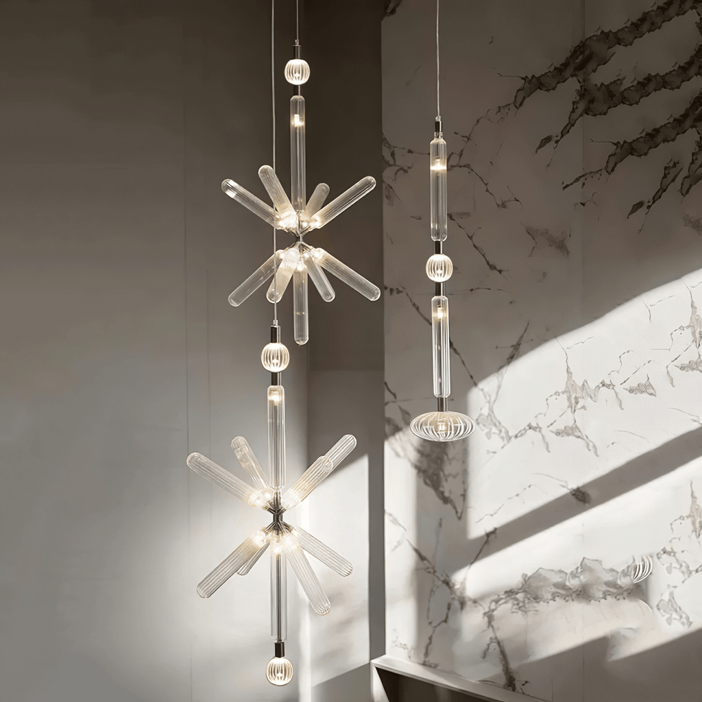 A crystal-burst Clérachic pendant and a linear one hang lit against a marble wall.