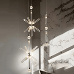 A crystal-burst Clérachic pendant and a linear one hang lit against a marble wall.