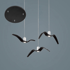 Three black bird-shaped pendants from this Clérachic fixture hang from a round black canopy, on a slate-blue backdrop.