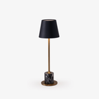 A slim brass stem rises from a black marble cylinder base to a black tapered shade on this Clérachic table lamp, photographed alone against a plain backdrop.