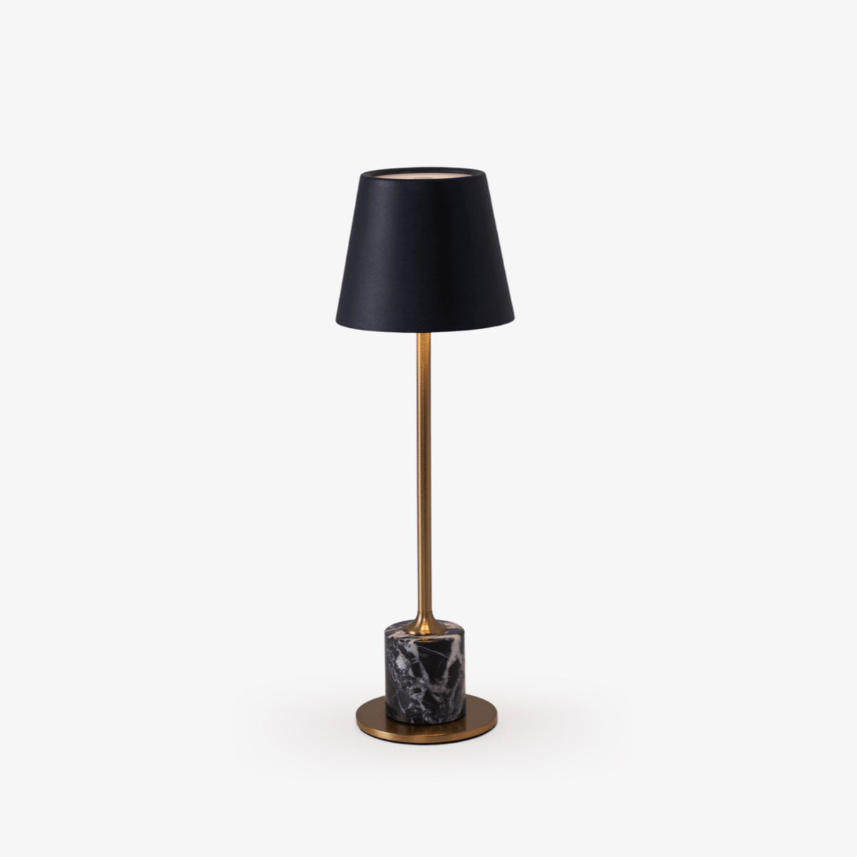 A slim brass stem rises from a black marble cylinder base to a black tapered shade on this Clérachic table lamp, photographed alone against a plain backdrop.