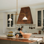 Beneath a copper range hood and white cabinetry, this Clérachic pendant glows warm above a kitchen island with fresh produce.