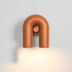 This terracotta Clérachic wall light glows warm on a plain grey backdrop, its twin spotlight heads lit.