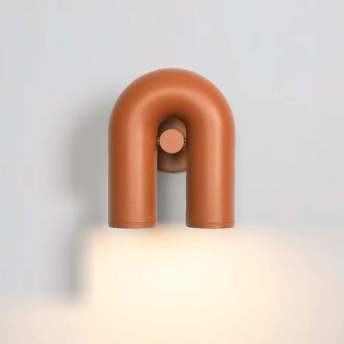 This terracotta Clérachic wall light glows warm on a plain grey backdrop, its twin spotlight heads lit.