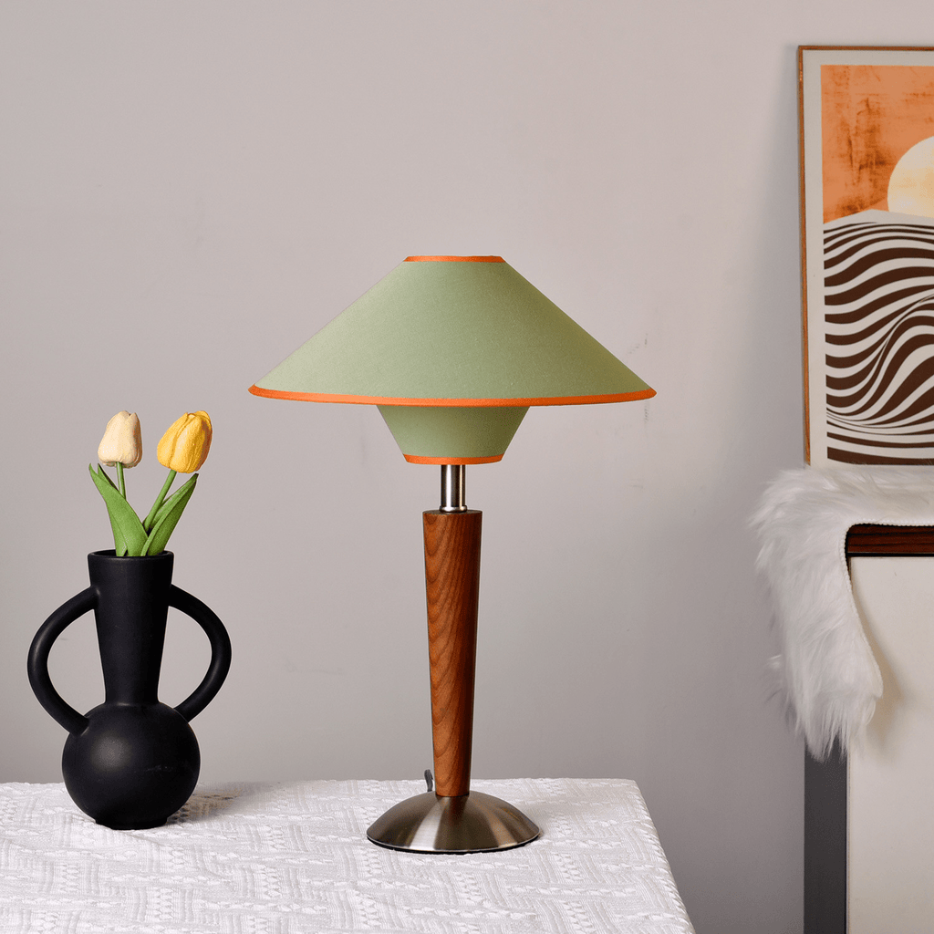 Tan fabric shade table lamp glowing beside a bed at night