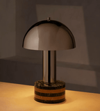 Same Clérachic lamp variant lit in warm evening light, its dark marble base and terracotta stripe glowing softly.