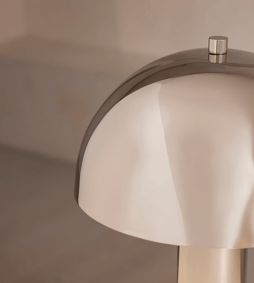 Macro crop of the Clérachic lamp's domed shade edge and finial, the polished metal reflecting the room around it.
