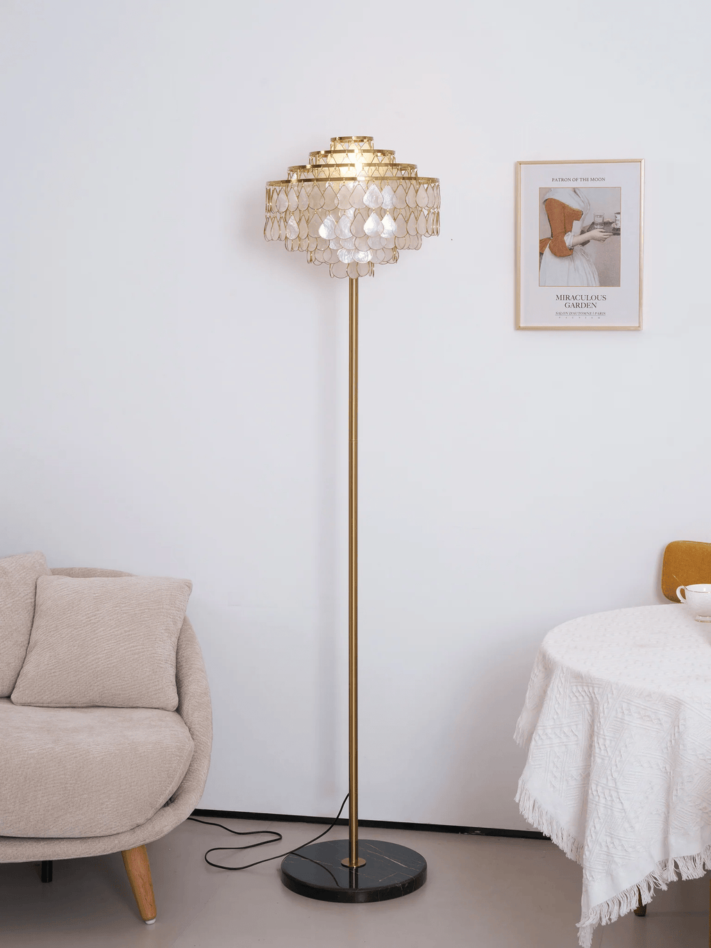 A round table draped in white linen sits beside this Clérachic floor lamp and a pale bouclé armchair.