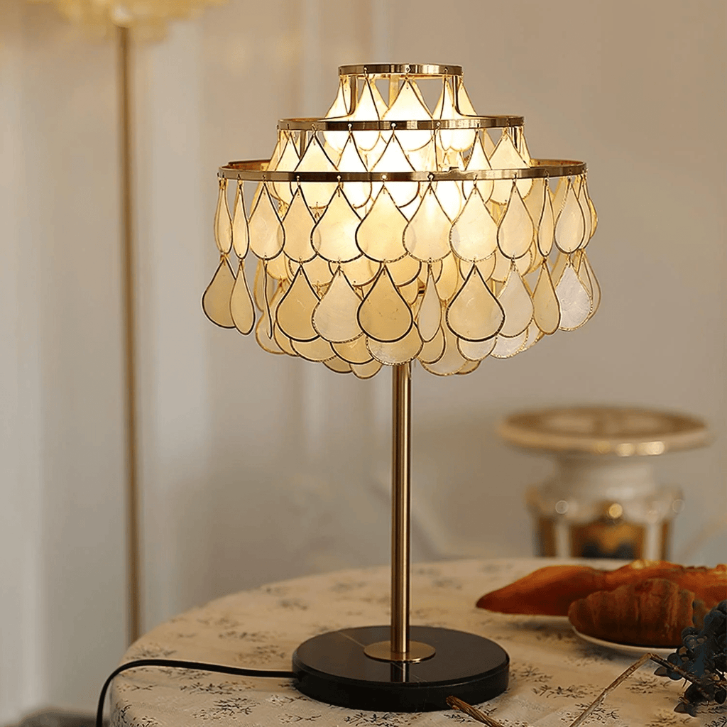 Close-up of the Clérachic lamp's shell teardrop shade glowing warm, with a blurred cake stand in the background.