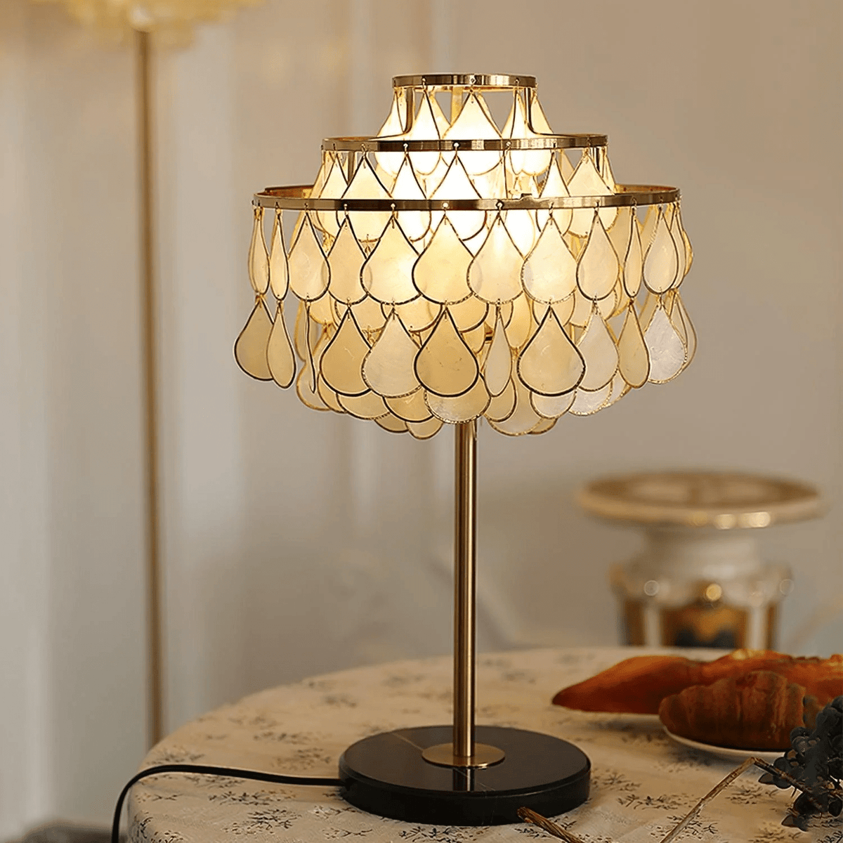 Close-up of the Clérachic lamp's shell teardrop shade glowing warm, with a blurred cake stand in the background.