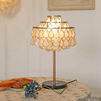 Clérachic table lamp glowing on a round table beside a loaf of bread and scattered blueberries on a floral cloth.
