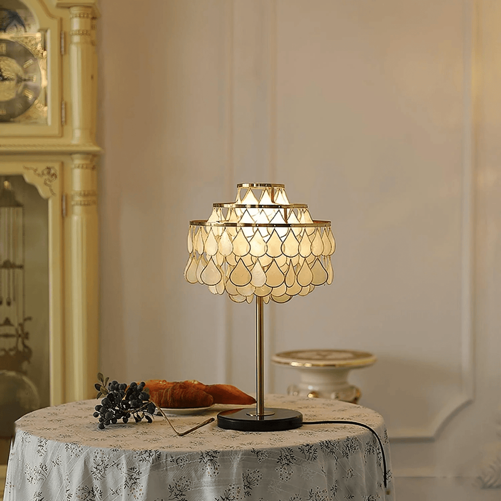 Clérachic table lamp glowing on a round floral-cloth table, a croissant plate and blueberries just beside its base.