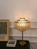 Near a gilt-framed picture on the wall, the Clérachic table lamp glows on a dark surface beside a small gift box.