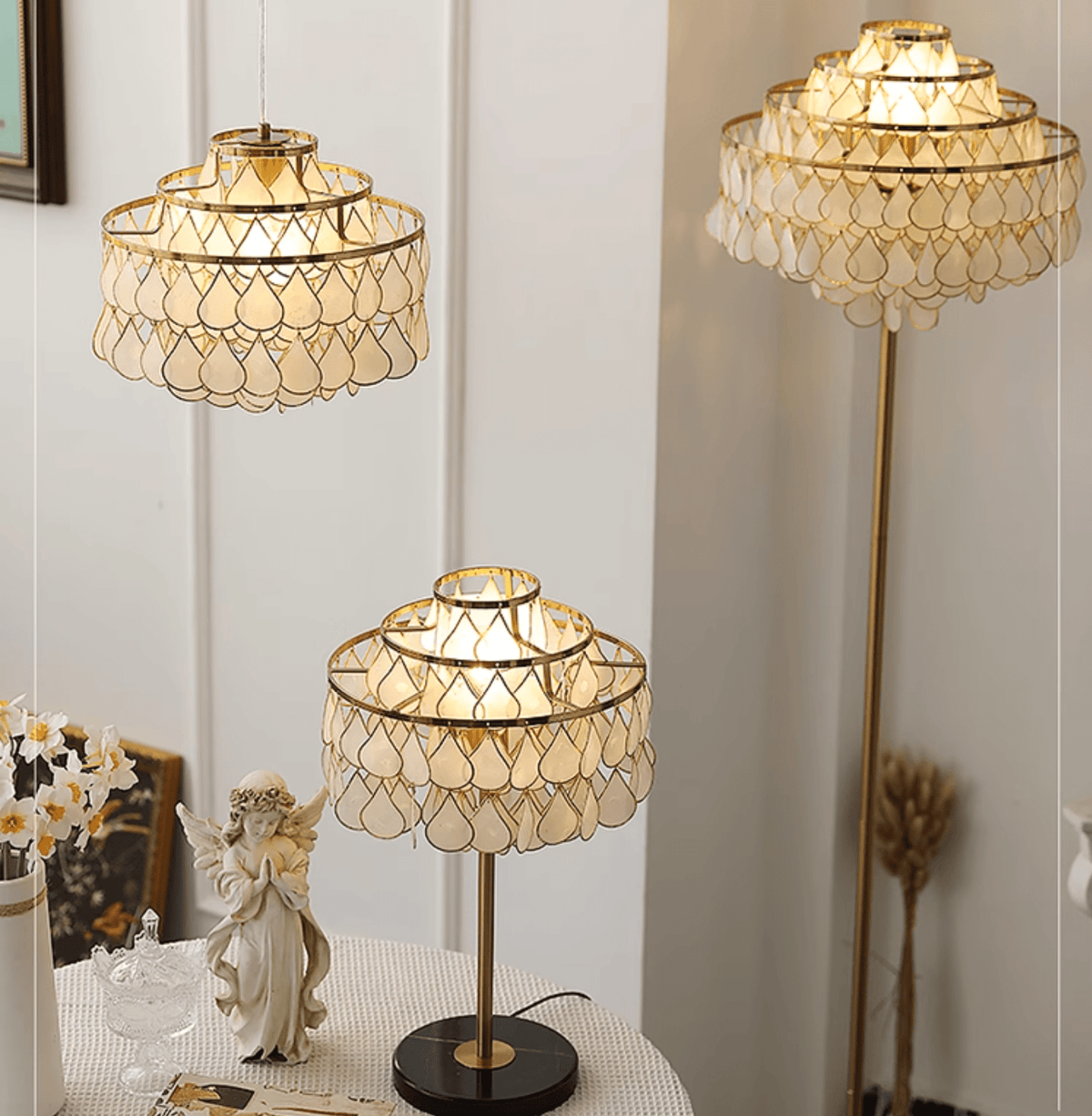 Clérachic table lamp glowing beside a porcelain angel figurine, with a matching pendant and floor lamp behind it.