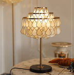 An ornate clock cabinet blurs behind the Clérachic table lamp, glowing on a round table with croissants and blueberries.
