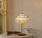 A marble stand blurs softly behind the Clérachic table lamp, glowing on a floral-cloth table with croissants and blueberries.