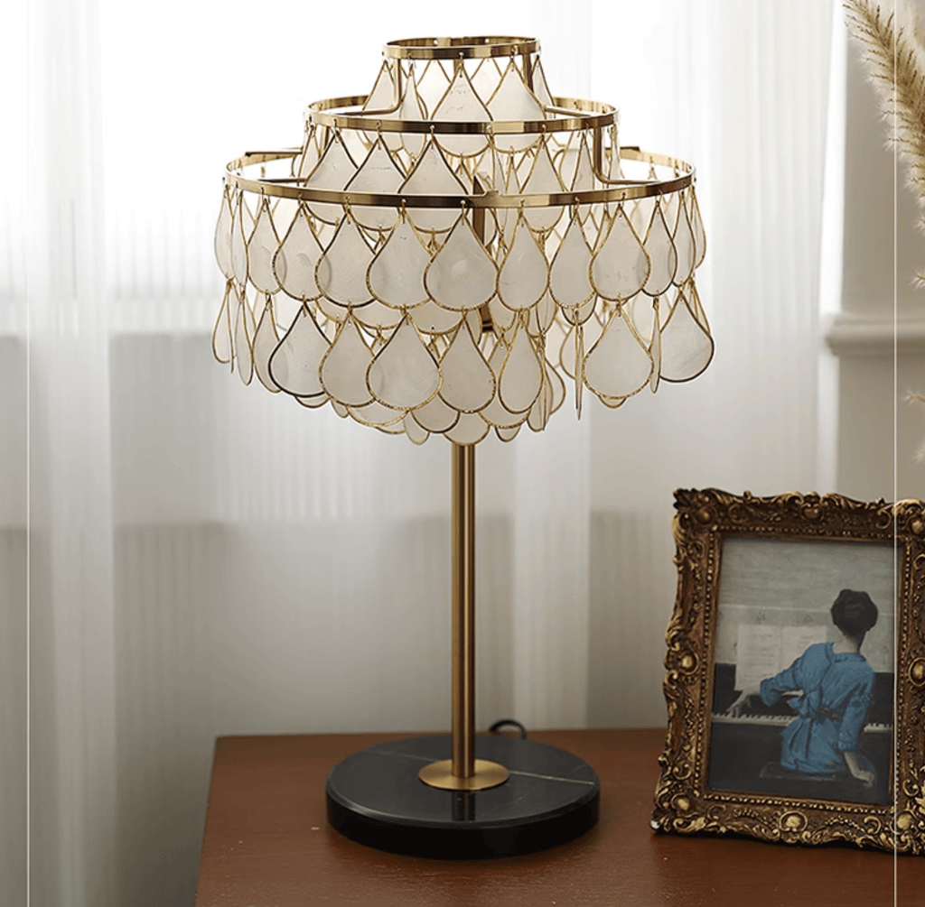 Close-up of the Clérachic table lamp glowing on a dark wood sideboard beside a vintage framed photograph.