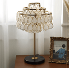 Close-up of the Clérachic table lamp glowing on a dark wood sideboard beside a vintage framed photograph.