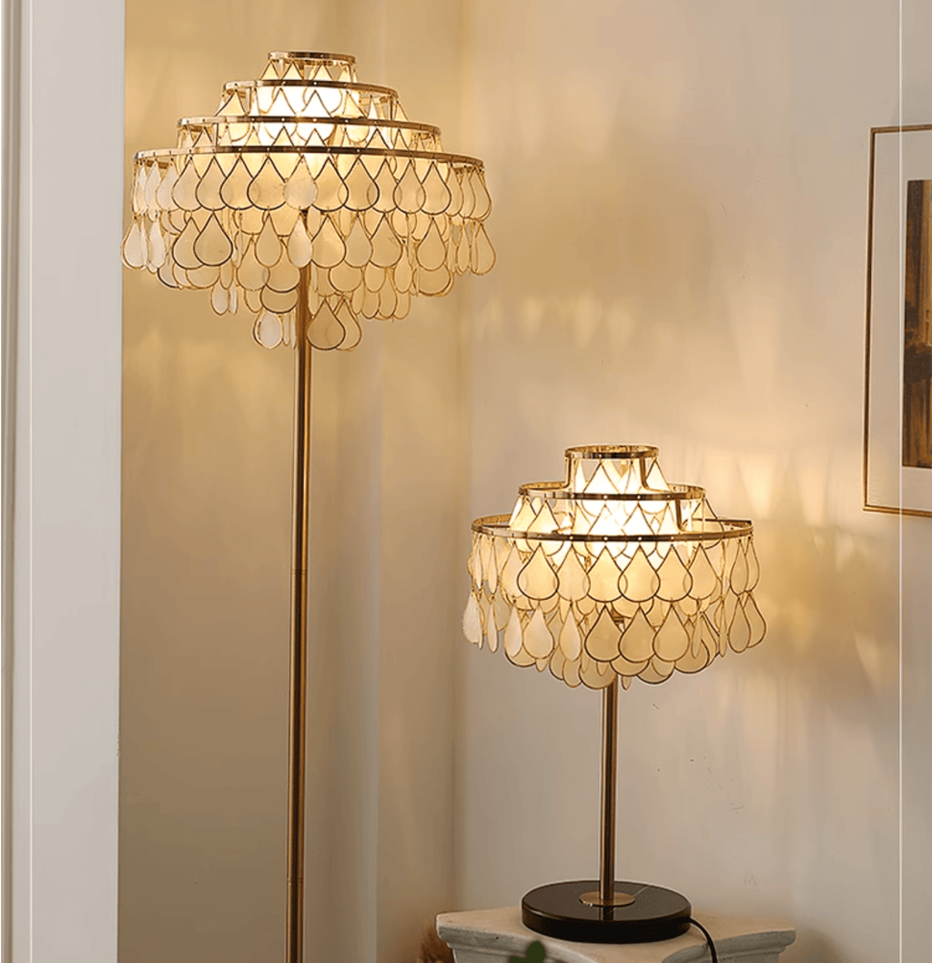 Clérachic table lamp and its taller floor-lamp companion glowing near a window, both set on dark wood surfaces.