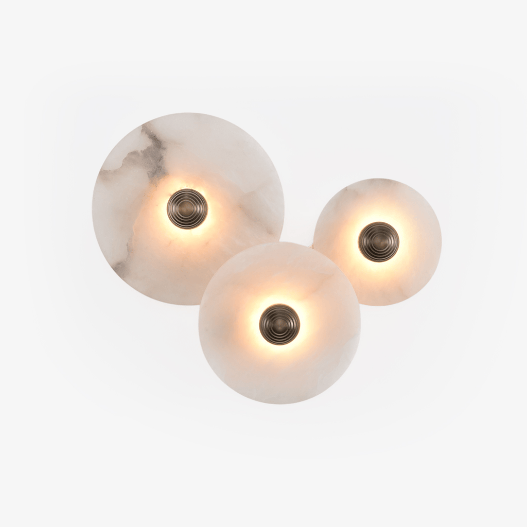 Three lit alabaster discs on a white wall, the largest showing a dark grey vein through the stone.